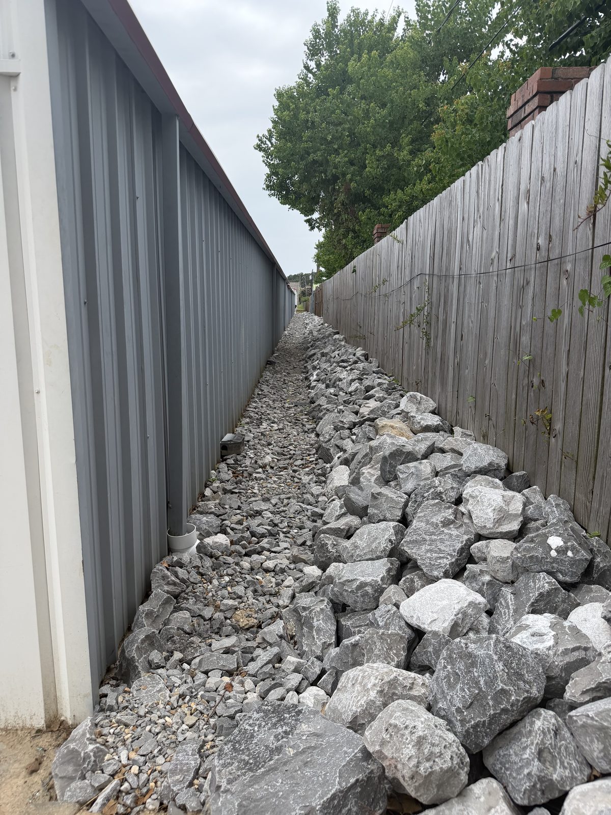 Completed rock-lined drainage channel running the length of the building