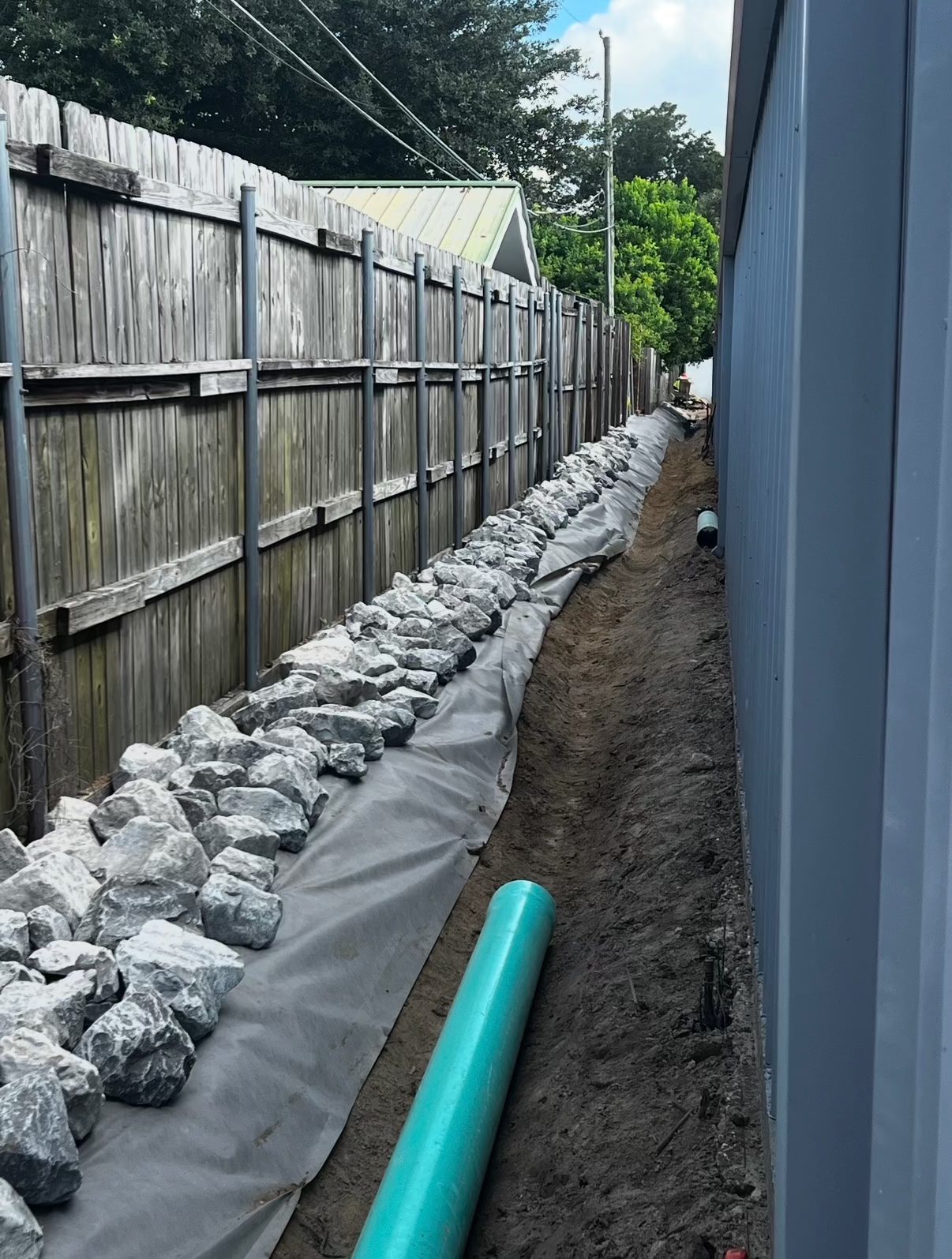 Filter fabric laid and riprap set along the fence with the drain line in the trench